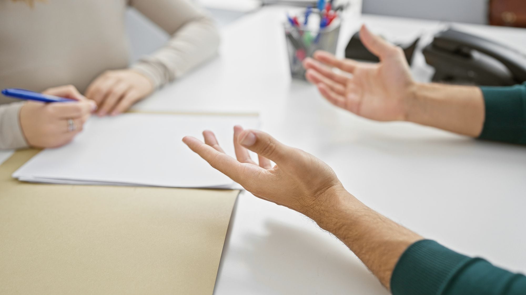 Two people in conversation across a table, one taking notes